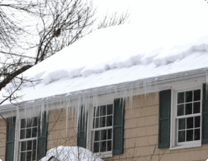 Snow-covered roof with icicles and ice dams forming along the eaves of a home. This photo shows how roof ice buildup occurs without gutter heat tape, emphasizing the importance of self-regulating heat cables like Heat Tape PRO to prevent water damage and keep gutters clear in winter.